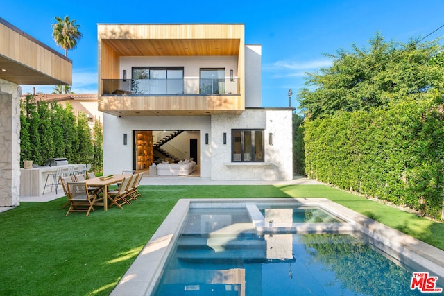 rear view of house with a balcony, exterior kitchen, a lawn, and a patio area