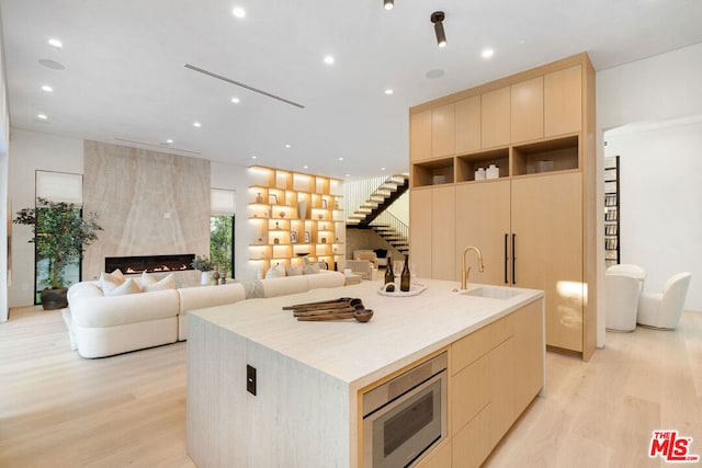 kitchen with sink, stainless steel microwave, a kitchen island with sink, and light brown cabinetry