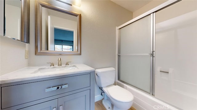 full bathroom with wood-type flooring, vanity, combined bath / shower with glass door, and toilet