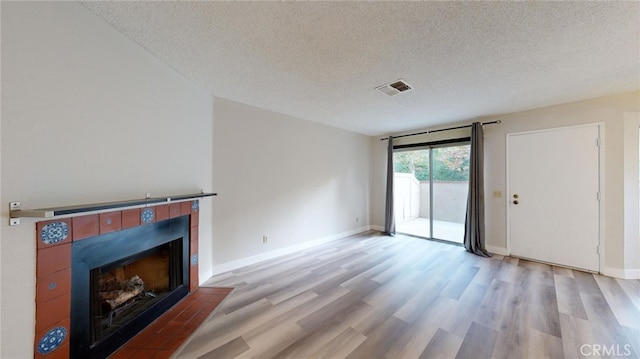 unfurnished living room featuring light hardwood / wood-style floors, a textured ceiling, and a tile fireplace