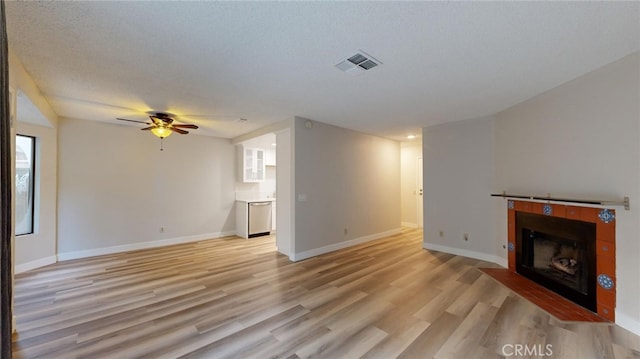 unfurnished living room featuring a textured ceiling, ceiling fan, light wood-type flooring, and a fireplace