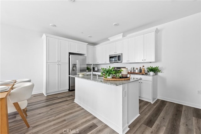 kitchen with white cabinets, stainless steel appliances, dark hardwood / wood-style floors, and a center island with sink