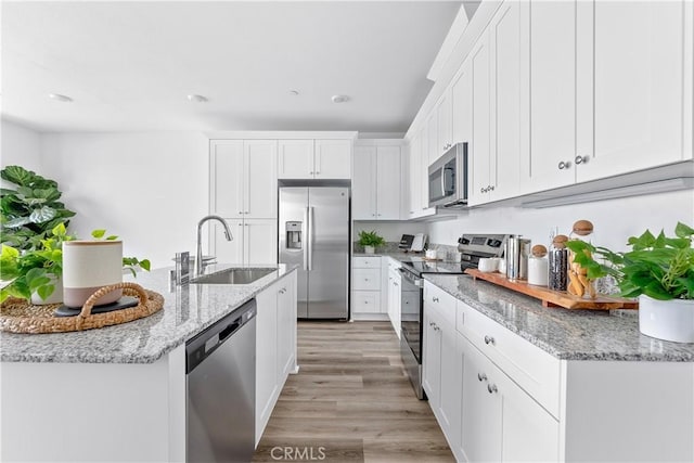 kitchen with light stone countertops, sink, stainless steel appliances, light hardwood / wood-style floors, and white cabinets