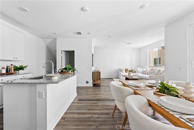 kitchen featuring white cabinets, stone countertops, and an island with sink