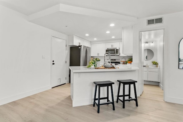 kitchen with kitchen peninsula, stainless steel appliances, white cabinetry, and light hardwood / wood-style floors