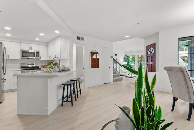 kitchen featuring kitchen peninsula, appliances with stainless steel finishes, light wood-type flooring, decorative backsplash, and white cabinetry