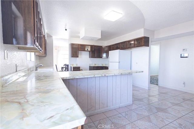 kitchen with kitchen peninsula, white refrigerator, dark brown cabinetry, and sink