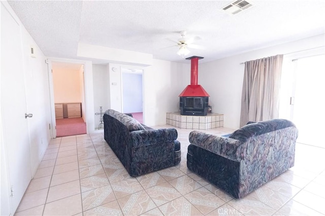 living room featuring a wood stove, ceiling fan, light tile patterned flooring, and a textured ceiling