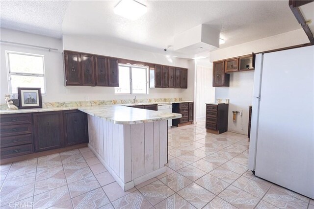 kitchen with kitchen peninsula, a textured ceiling, dark brown cabinetry, light tile patterned floors, and white refrigerator