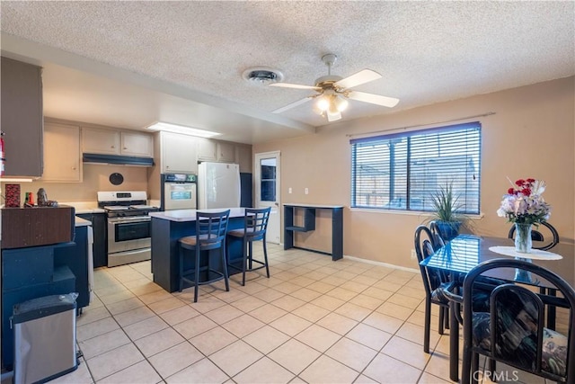 kitchen with a breakfast bar area, light tile patterned floors, ceiling fan, and white appliances