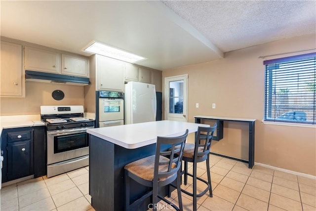 kitchen featuring a center island, white appliances, a textured ceiling, a breakfast bar area, and light tile patterned floors