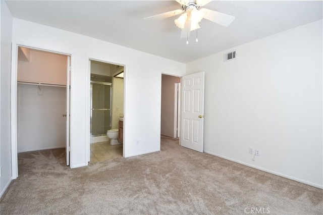 unfurnished bedroom with light carpet, a walk in closet, ensuite bath, and ceiling fan