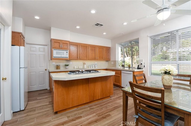 kitchen featuring a center island, white appliances, ceiling fan, light wood-type flooring, and tasteful backsplash