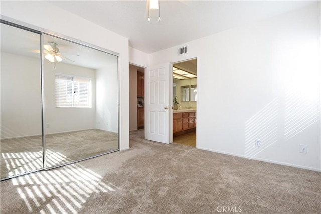 unfurnished bedroom featuring ceiling fan, light carpet, connected bathroom, and a closet