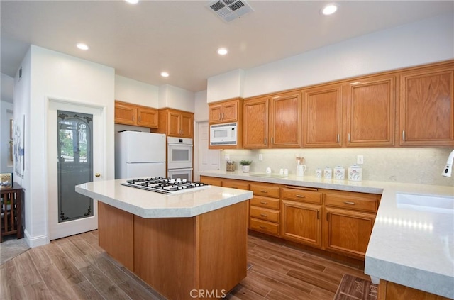 kitchen featuring hardwood / wood-style floors, white appliances, a center island, and backsplash