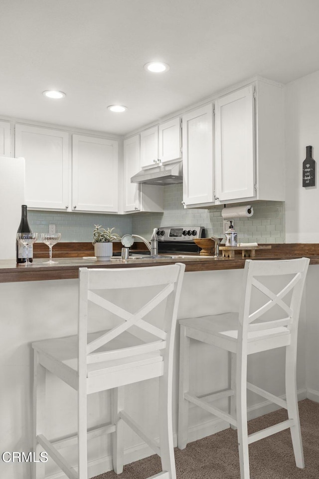 kitchen featuring a kitchen bar, tasteful backsplash, electric stove, carpet floors, and white cabinetry