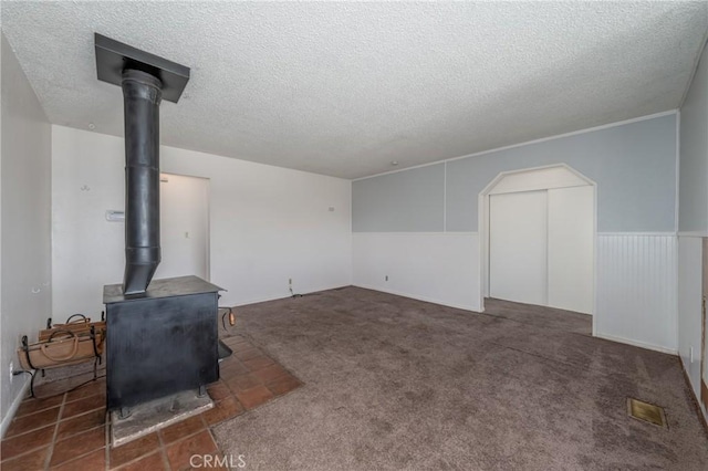 unfurnished living room with a wood stove, dark carpet, and a textured ceiling