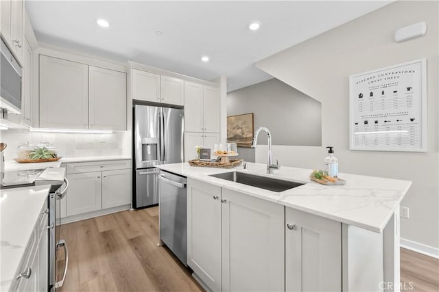 kitchen featuring stainless steel appliances, a kitchen island with sink, sink, white cabinets, and light hardwood / wood-style floors