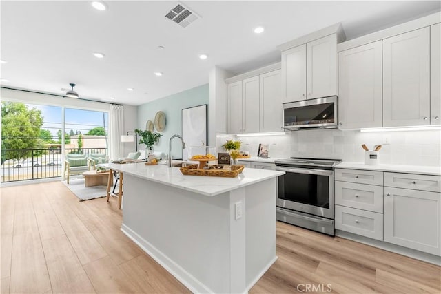 kitchen featuring light wood-type flooring, stainless steel appliances, sink, a center island with sink, and white cabinetry