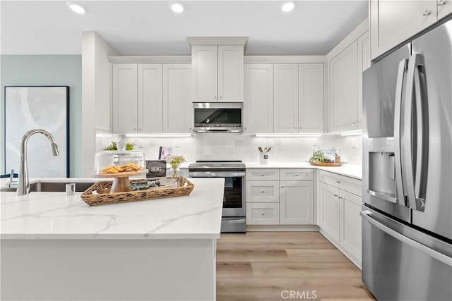 kitchen with tasteful backsplash, light hardwood / wood-style floors, light stone counters, white cabinetry, and stainless steel appliances