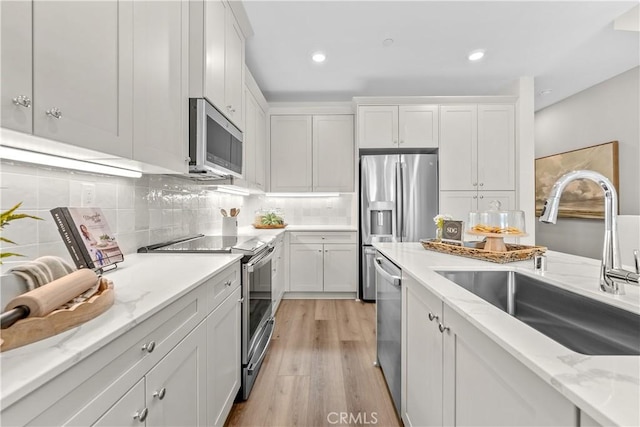 kitchen with white cabinets, sink, light hardwood / wood-style floors, light stone counters, and stainless steel appliances