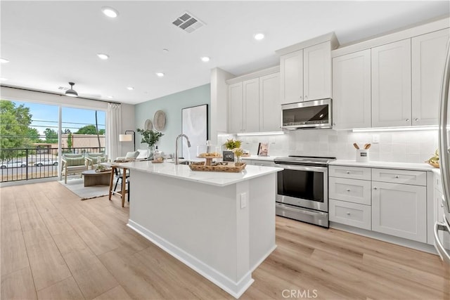 kitchen with a kitchen island with sink, white cabinets, stainless steel appliances, and light wood-type flooring