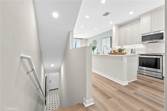 interior space with decorative backsplash, light wood-type flooring, stainless steel appliances, a kitchen island with sink, and white cabinetry