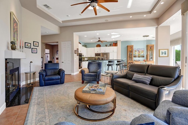 living room with ceiling fan, light tile patterned floors, a fireplace, and a tray ceiling