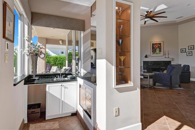 bar with ceiling fan, sink, dark tile patterned floors, a tiled fireplace, and white cabinets