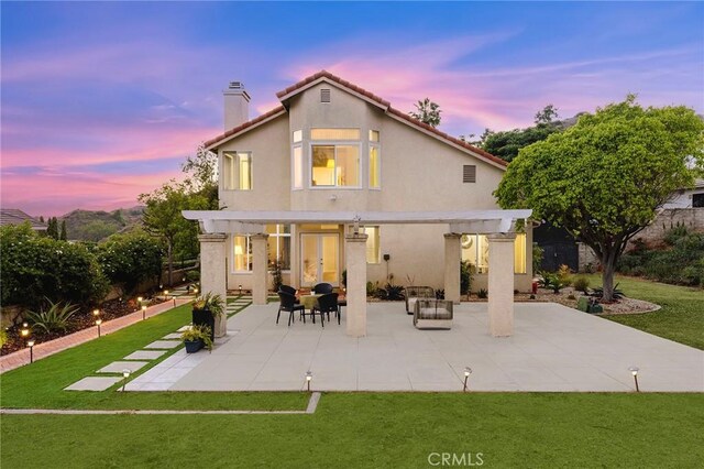 back house at dusk with a pergola and a yard