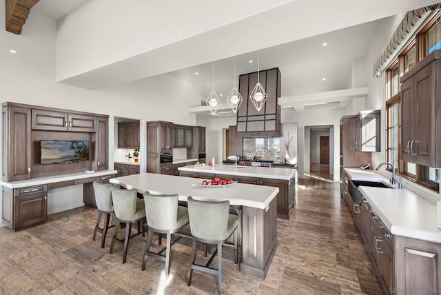 kitchen featuring a towering ceiling, a spacious island, sink, hanging light fixtures, and a breakfast bar area