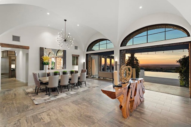 dining space featuring an inviting chandelier, high vaulted ceiling, a water view, and light hardwood / wood-style flooring