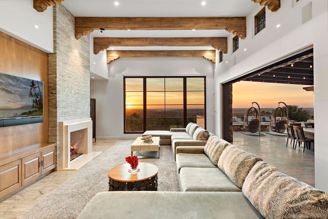 living room featuring a stone fireplace, beamed ceiling, and a high ceiling