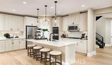 kitchen featuring decorative light fixtures, light wood-type flooring, stainless steel appliances, and a kitchen island with sink