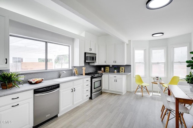 kitchen featuring appliances with stainless steel finishes, tasteful backsplash, sink, white cabinets, and light hardwood / wood-style floors