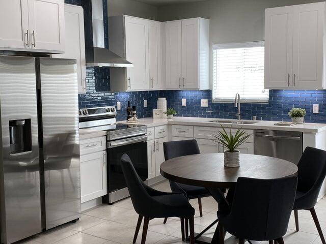 kitchen with tasteful backsplash, wall chimney exhaust hood, stainless steel appliances, sink, and white cabinets