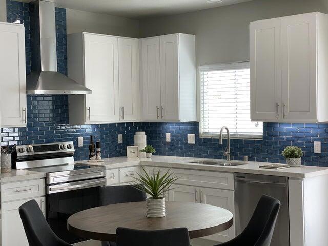 kitchen with white cabinets, appliances with stainless steel finishes, wall chimney exhaust hood, and sink