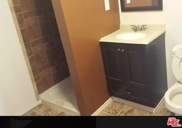 bathroom featuring a tile shower, vanity, and toilet