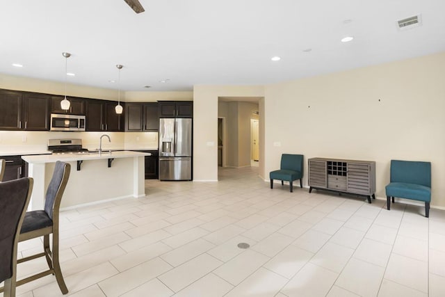 kitchen featuring a kitchen bar, dark brown cabinets, stainless steel appliances, a kitchen island with sink, and decorative light fixtures