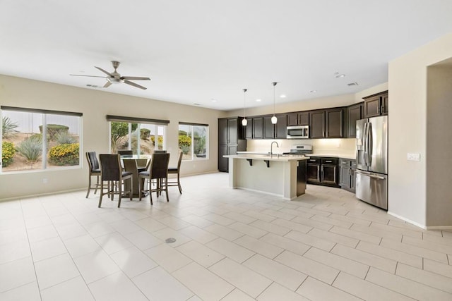 kitchen featuring ceiling fan, an island with sink, pendant lighting, a kitchen bar, and appliances with stainless steel finishes