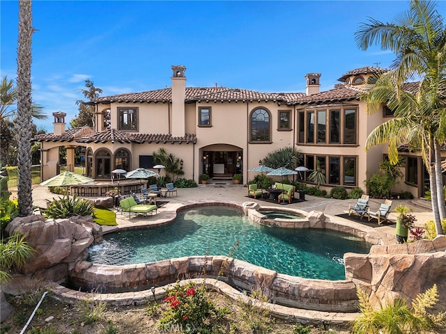 rear view of house with a swimming pool with hot tub and a patio