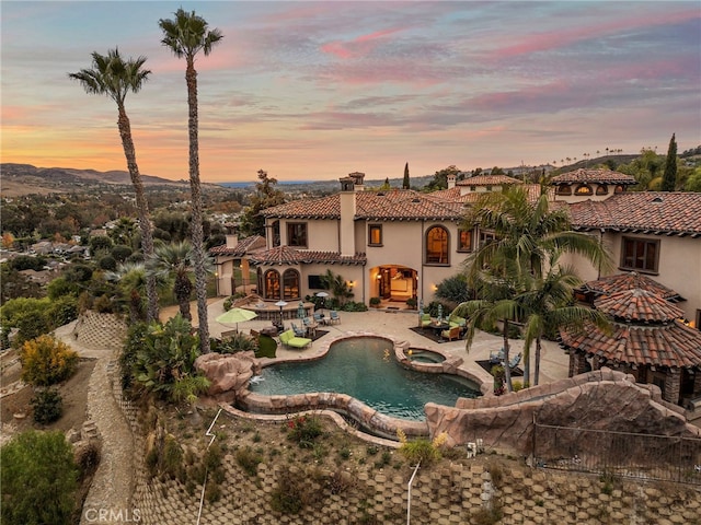 pool at dusk with a patio area and an in ground hot tub