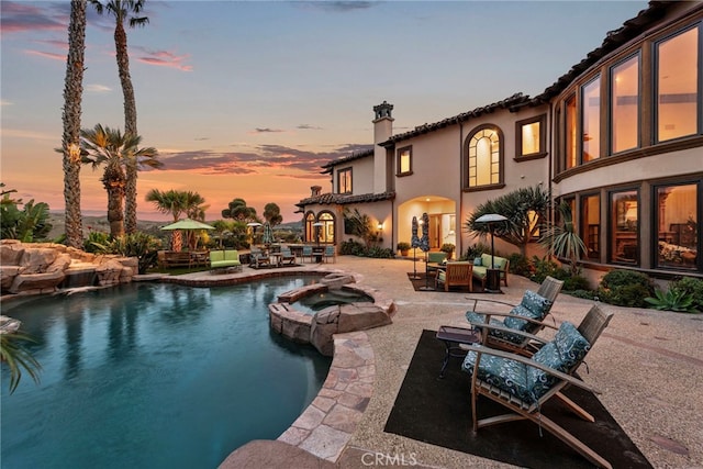 pool at dusk featuring an in ground hot tub and a patio