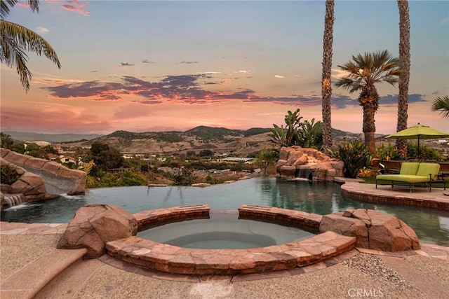 pool at dusk with an in ground hot tub, pool water feature, and a mountain view