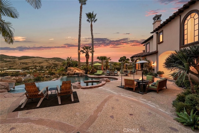 patio terrace at dusk featuring a mountain view and a pool with hot tub