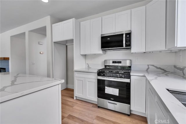 kitchen with light stone counters, light hardwood / wood-style flooring, white cabinets, and appliances with stainless steel finishes