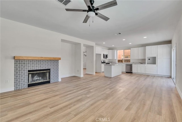 unfurnished living room featuring light hardwood / wood-style flooring, ceiling fan, and a tiled fireplace