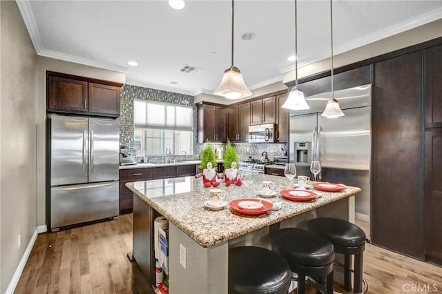 kitchen featuring dark brown cabinetry, a center island, stainless steel appliances, light stone counters, and light hardwood / wood-style floors