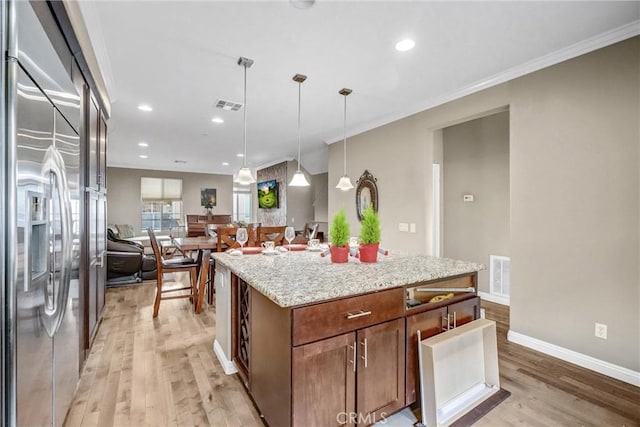 kitchen with crown molding, decorative light fixtures, light hardwood / wood-style floors, a kitchen island, and built in fridge