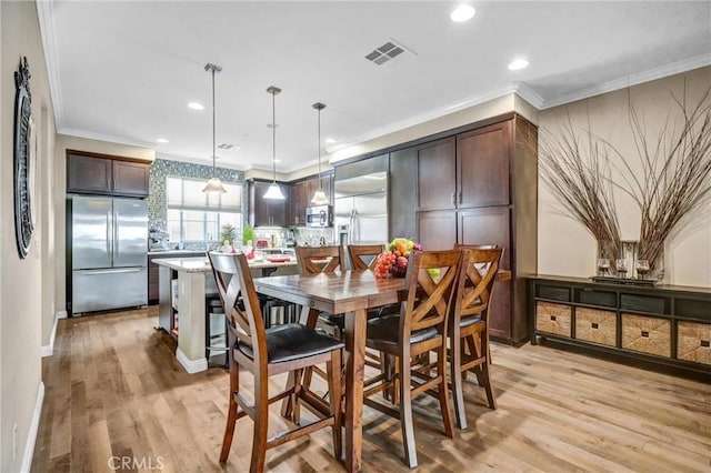 dining space featuring light wood-type flooring and crown molding